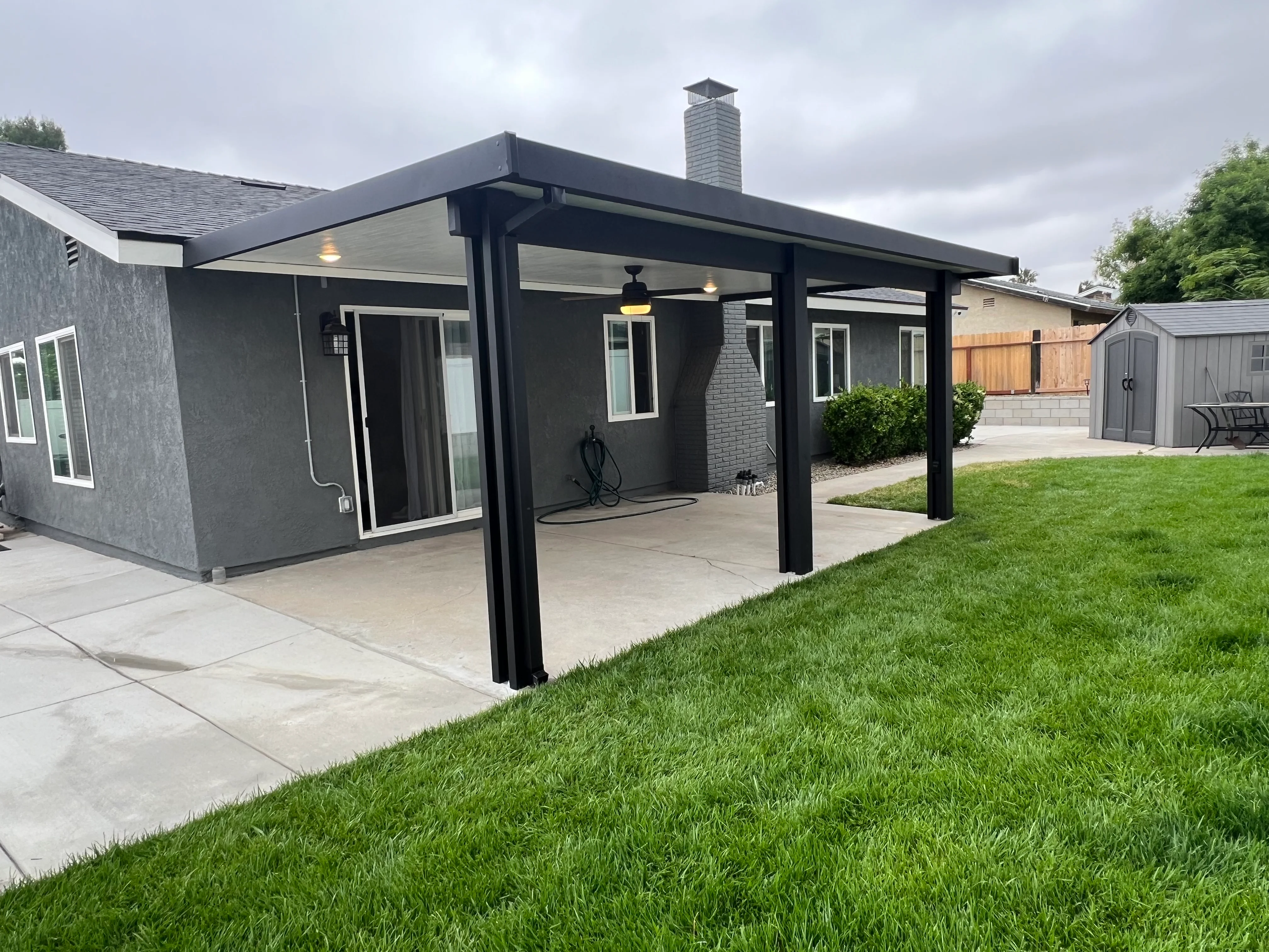 Black aluminum patio cover with ceiling lights over concrete patio beside gray modern home