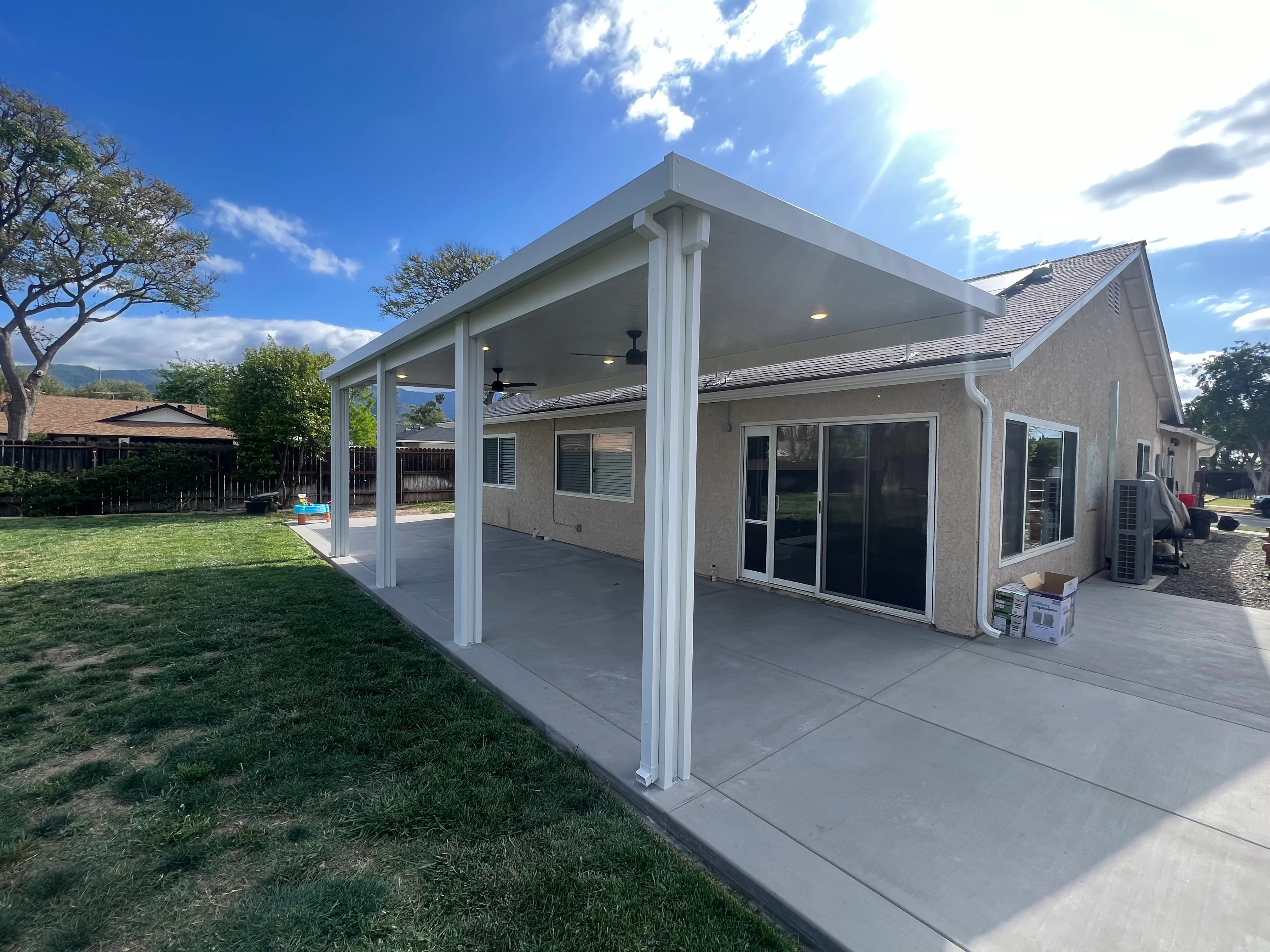 White aluminum patio cover with columns attached to stucco home with concrete pad
