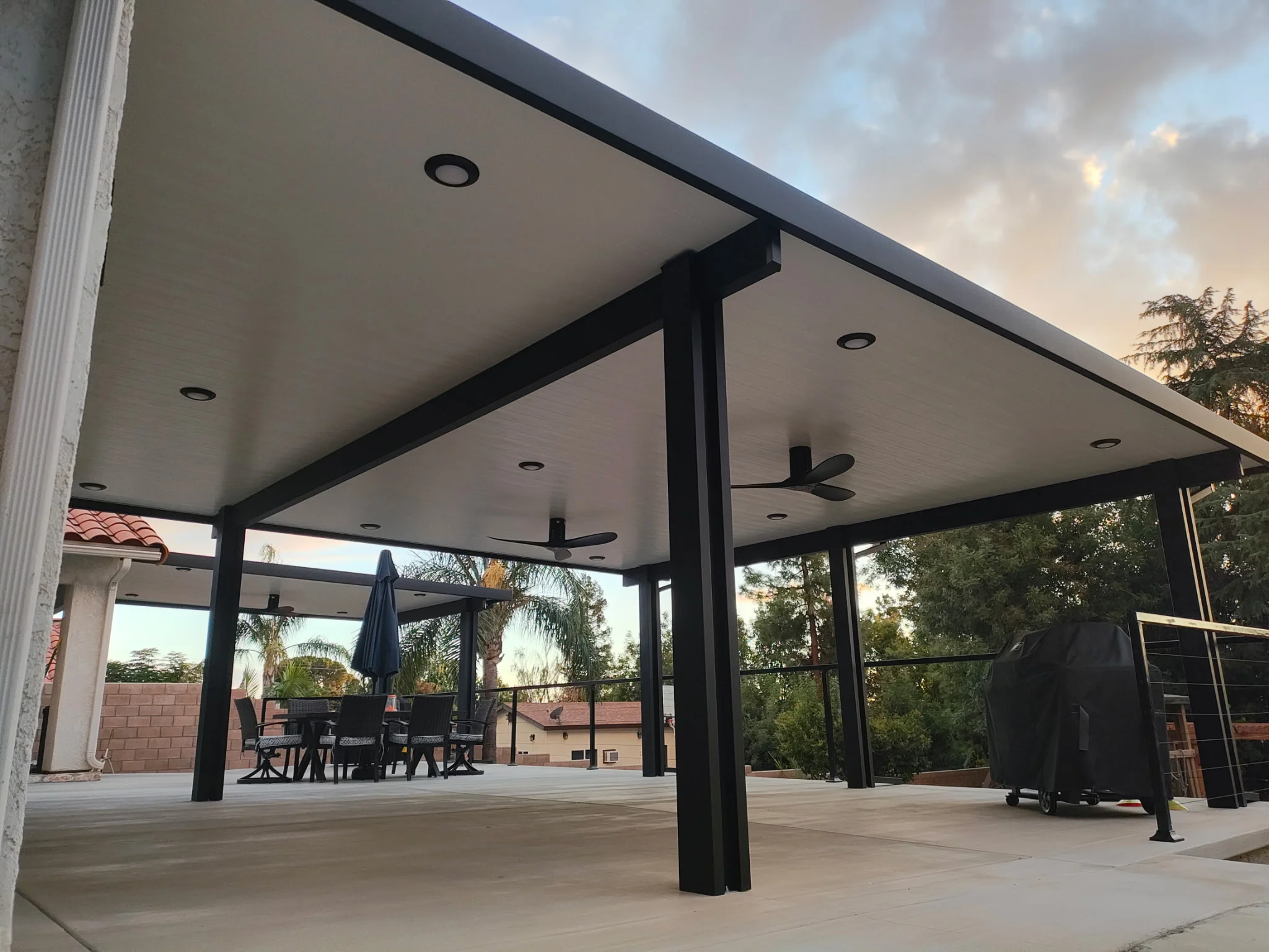Modern patio cover with black beams, white ceiling, recessed lights, and glass panels