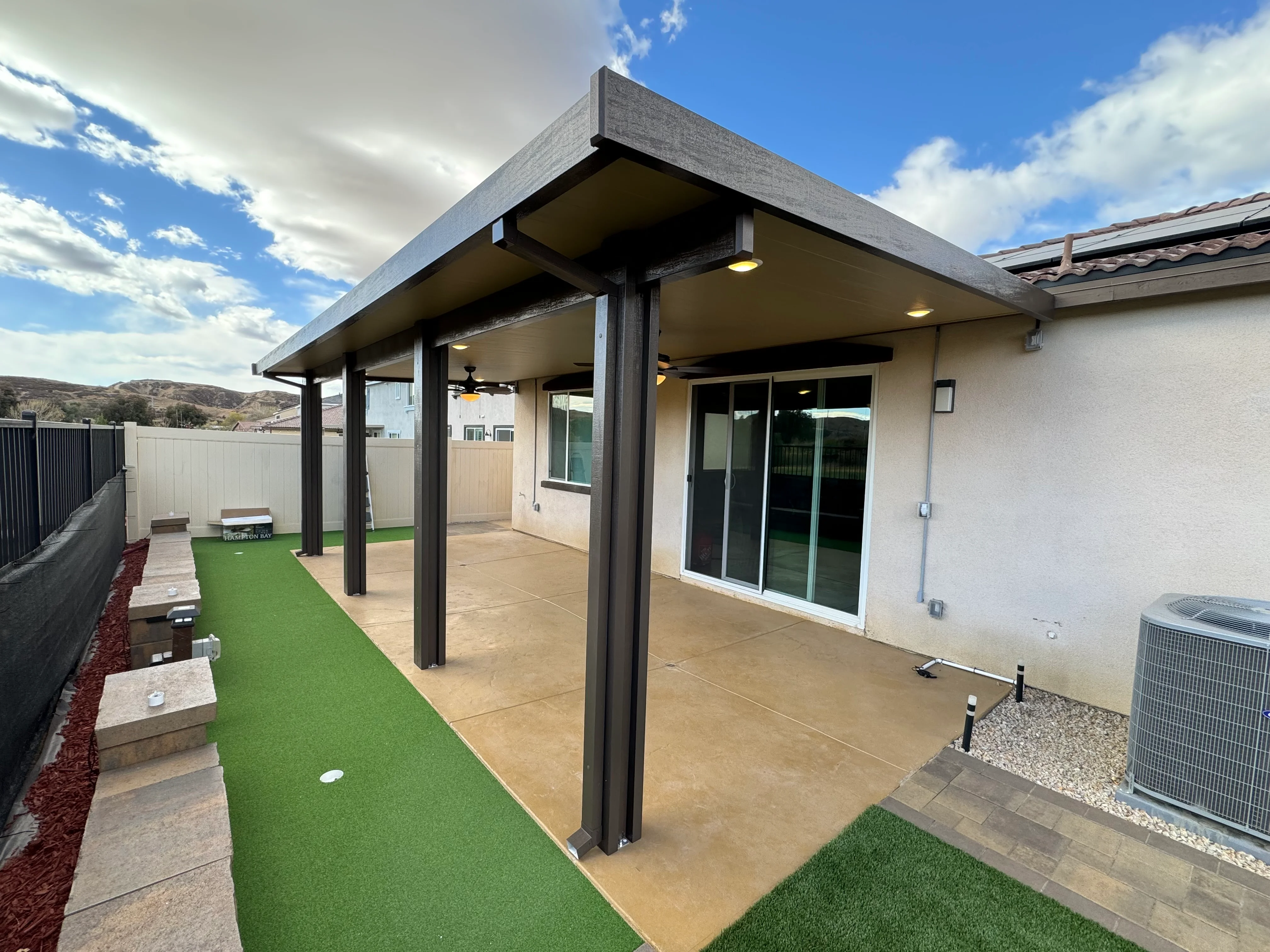 Modern patio cover with dark aluminum frame, recessed lighting, concrete patio, and synthetic turf