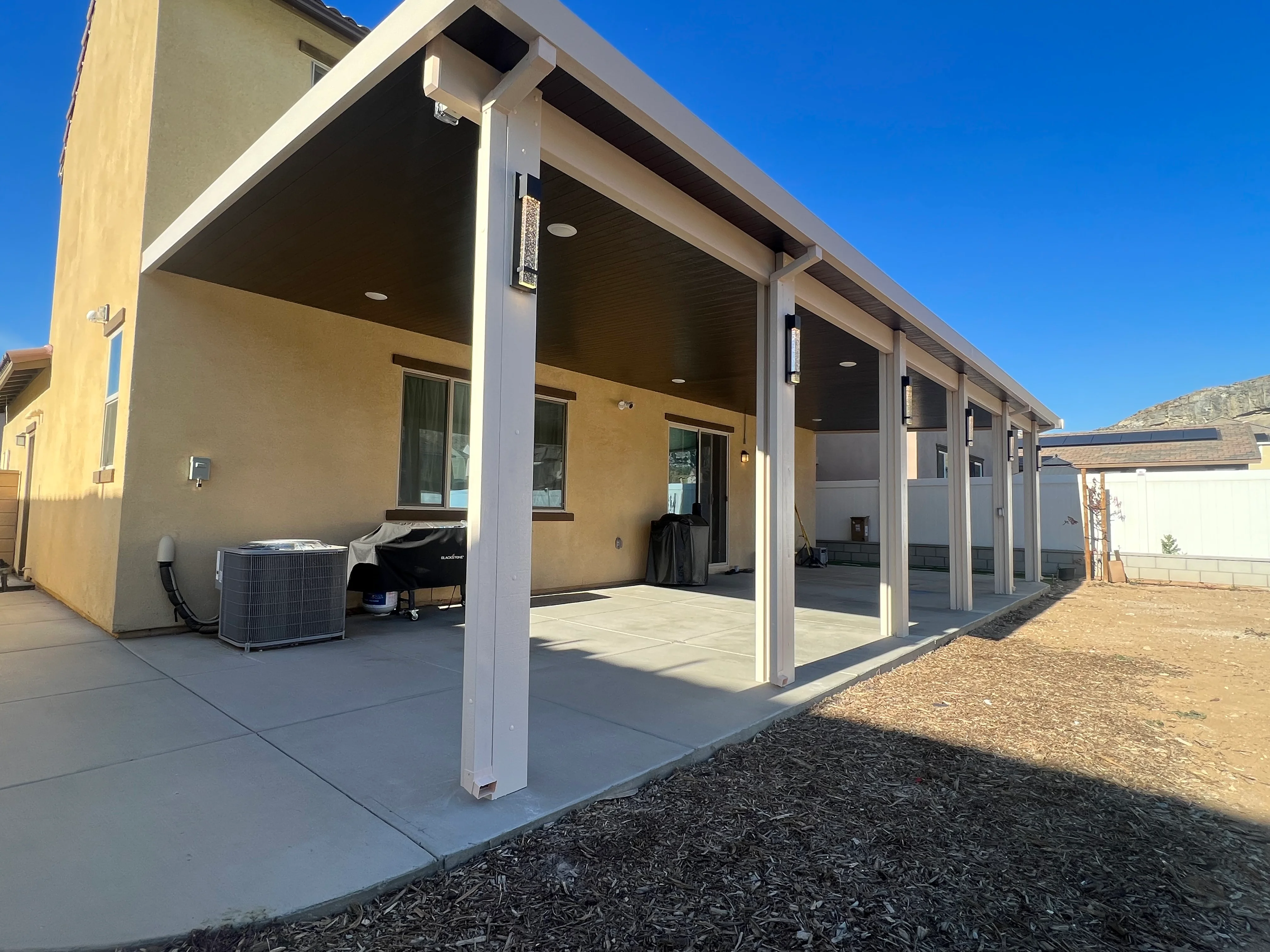 White aluminum patio cover with dark soffit over concrete patio adjacent to modern home