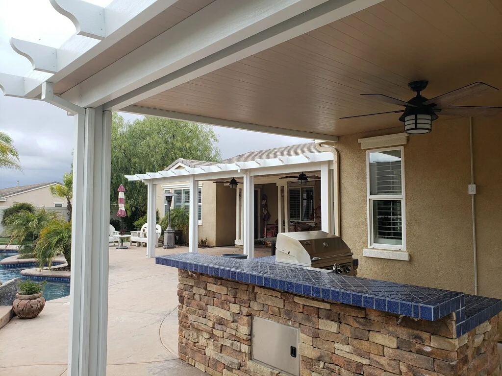 Modern covered patio with aluminum roof, skylights, ceiling fan, and stone outdoor kitchen island