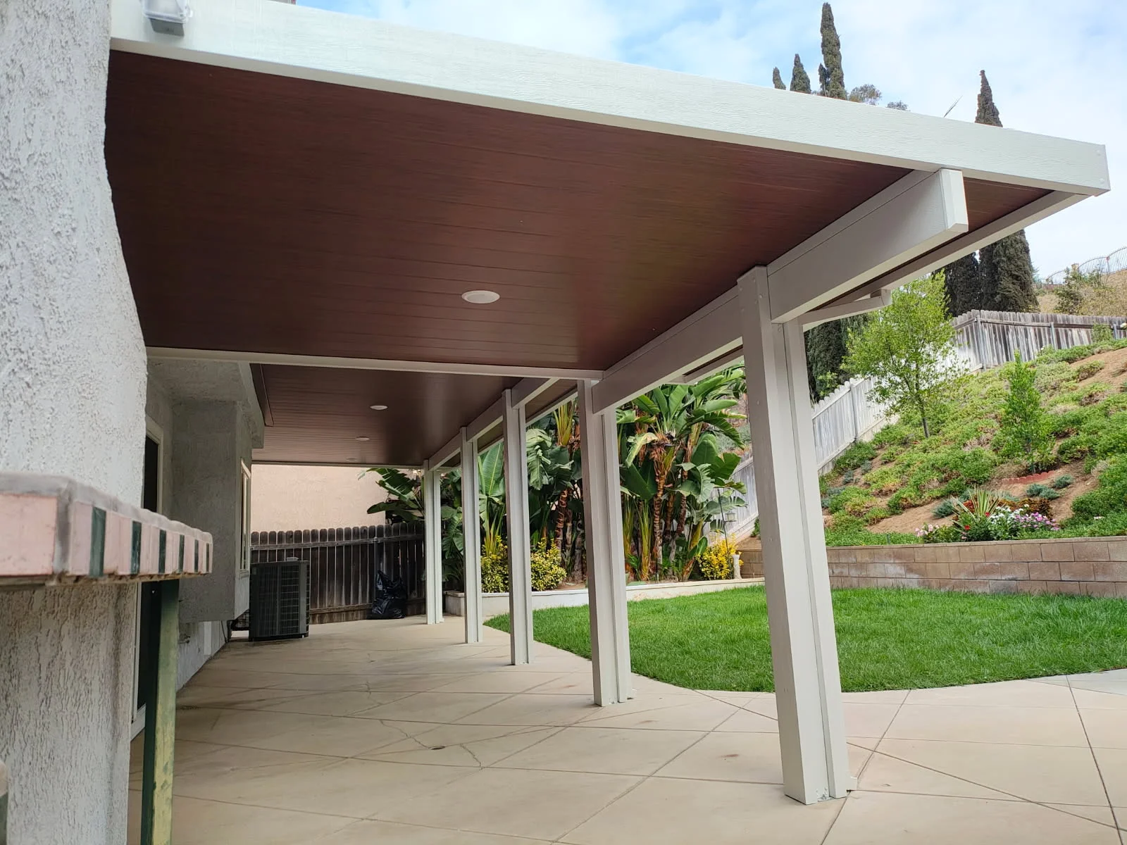 Modern patio cover with dark wood ceiling and white aluminum posts over concrete patio