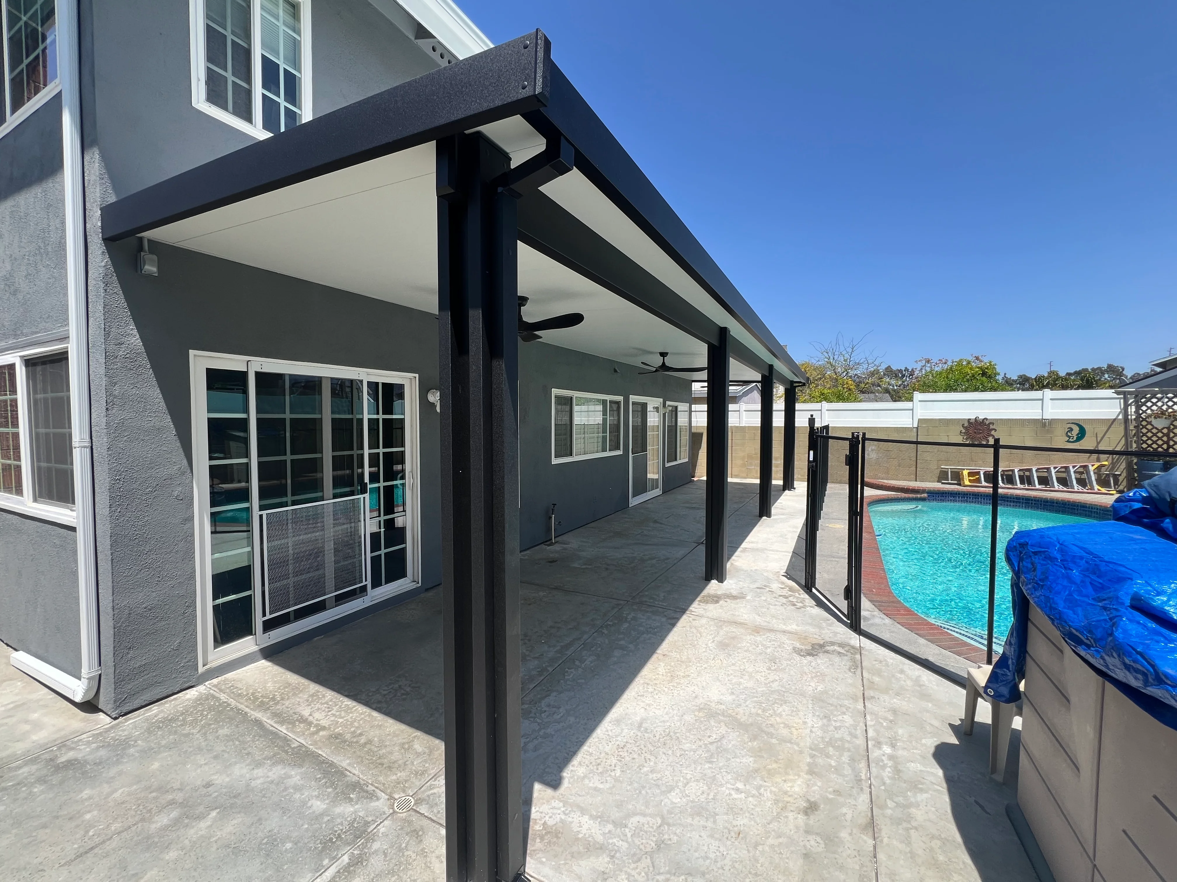 Black aluminum patio cover with shade panels overlooking swimming pool and deck area