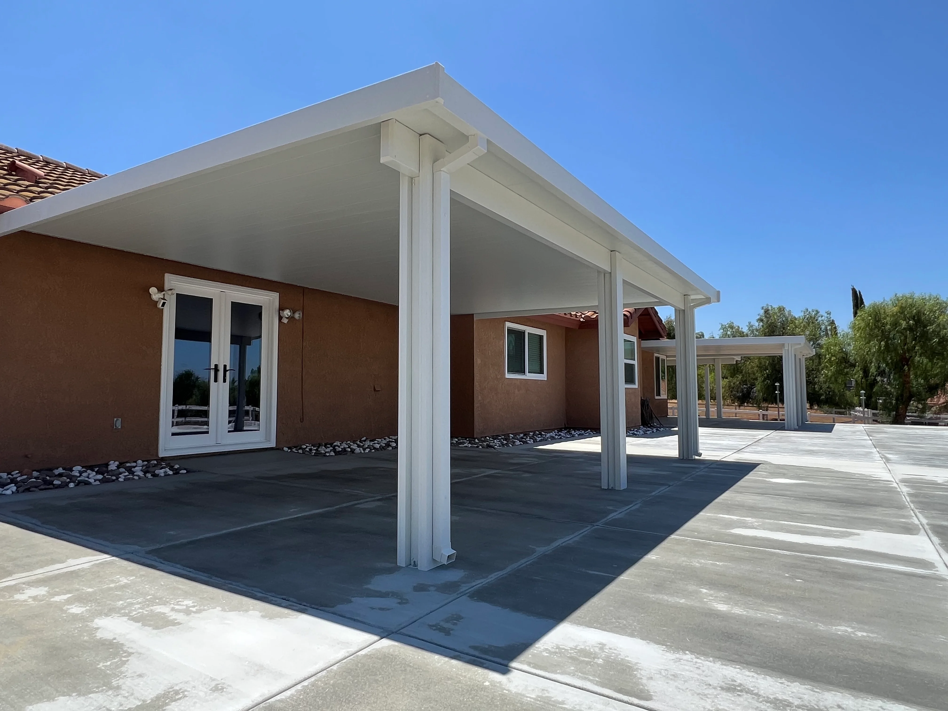 White aluminum patio cover with columns over concrete pad beside brick home