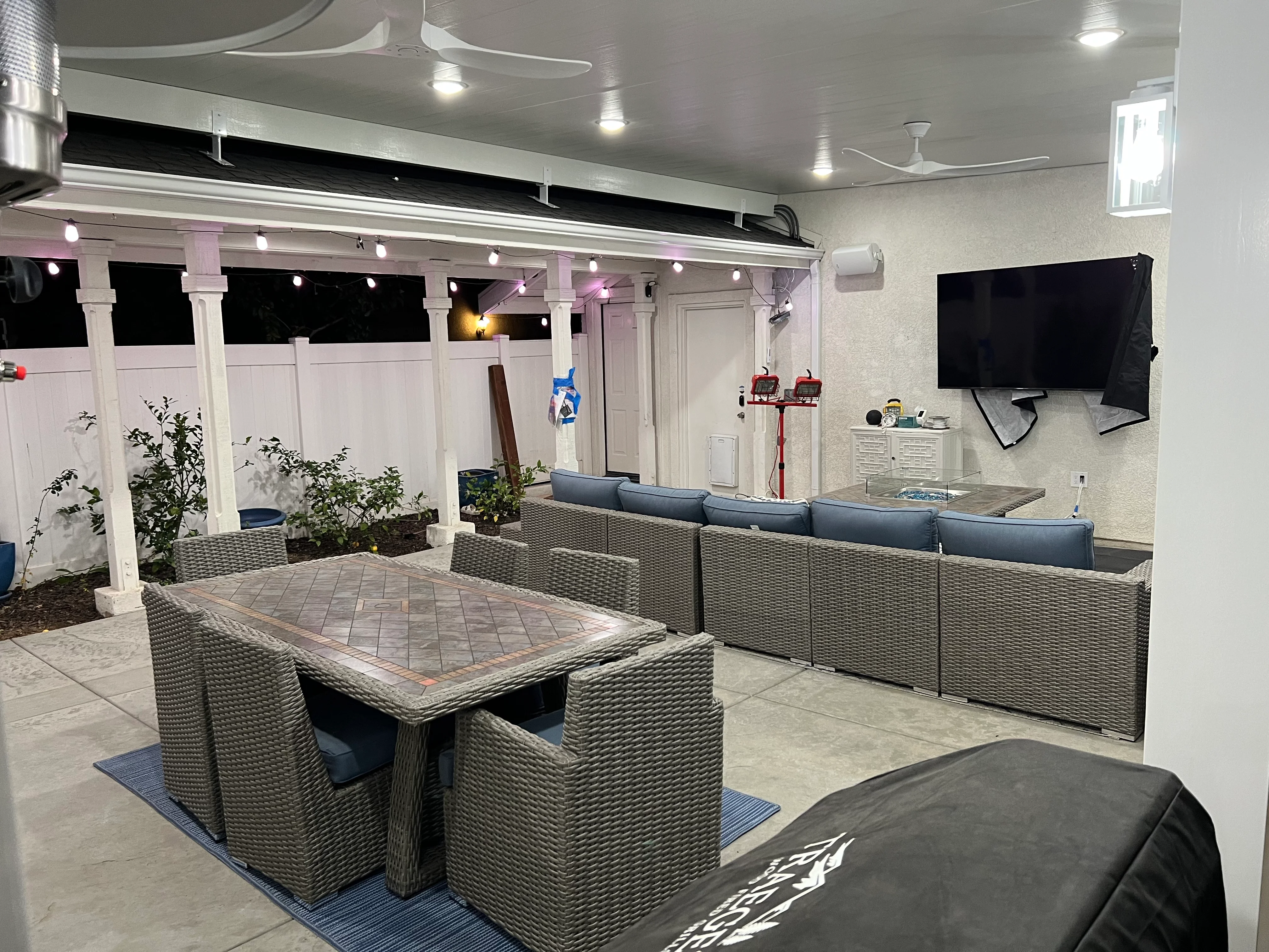 Modern covered patio with white pergola, wicker furniture, LED lighting, and concrete flooring