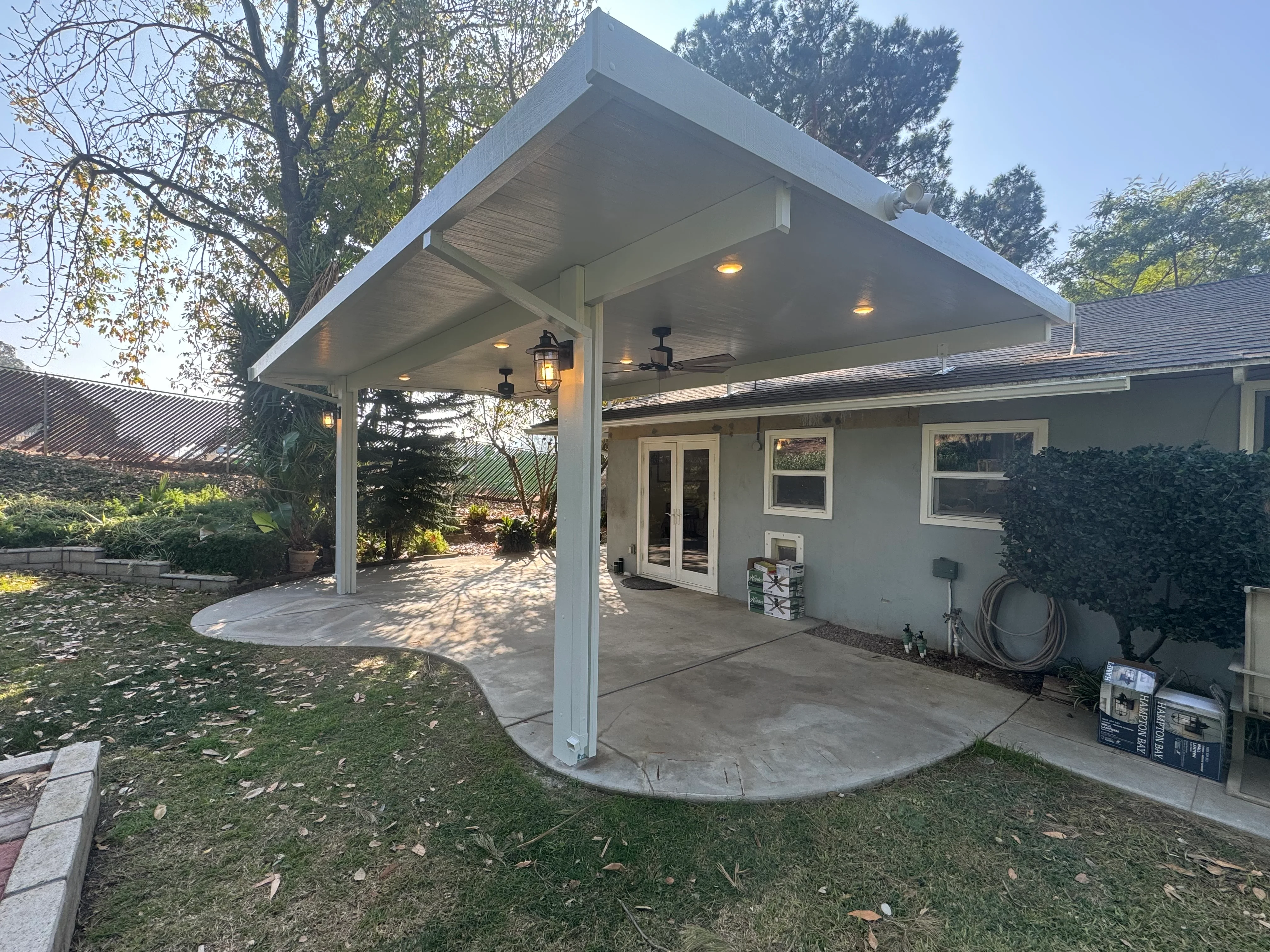 White aluminum patio cover with ceiling fans and recessed lighting over concrete pad