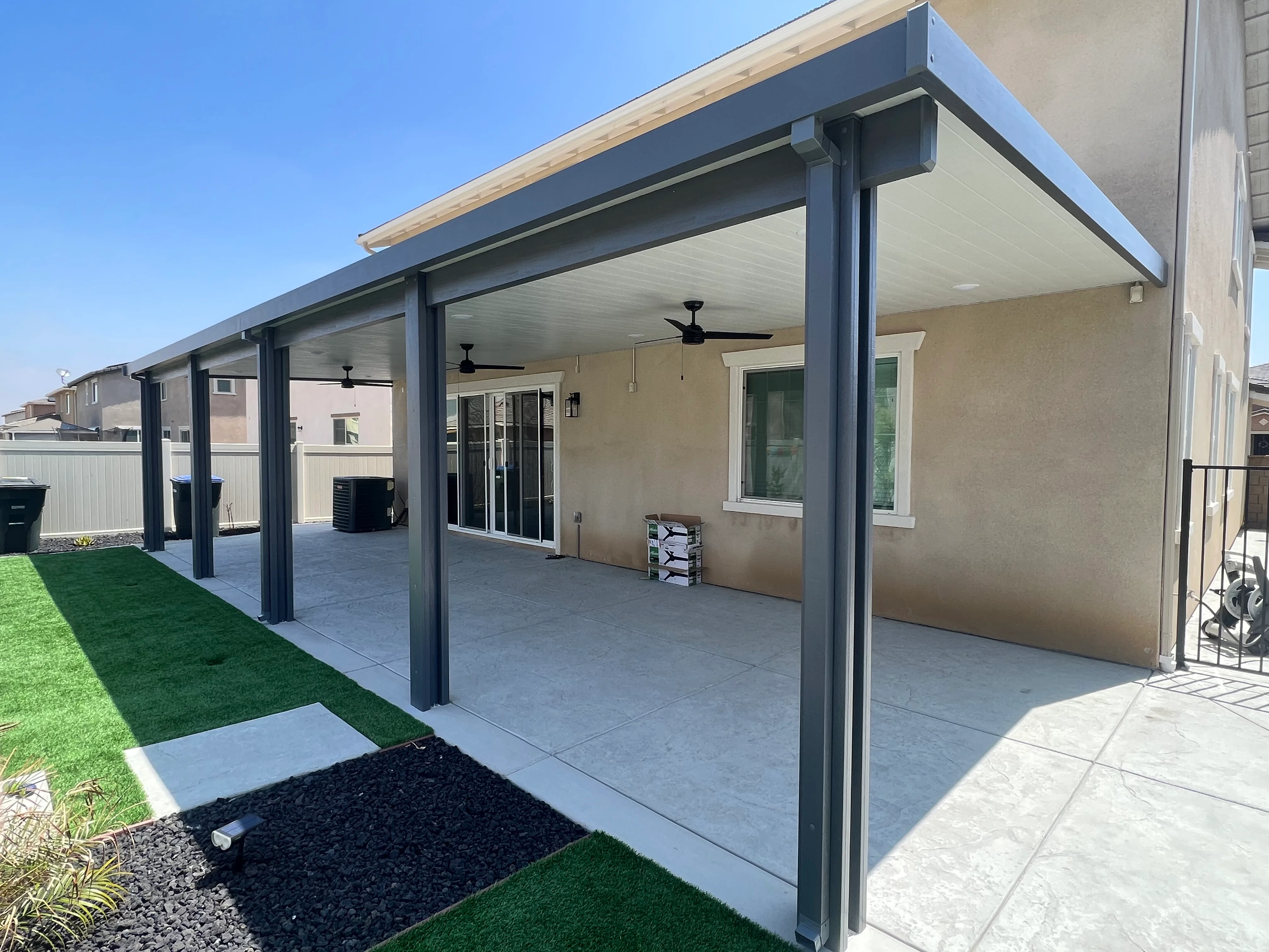 Modern patio cover with dark metal frame, white ceiling, and ceiling fans over concrete pad