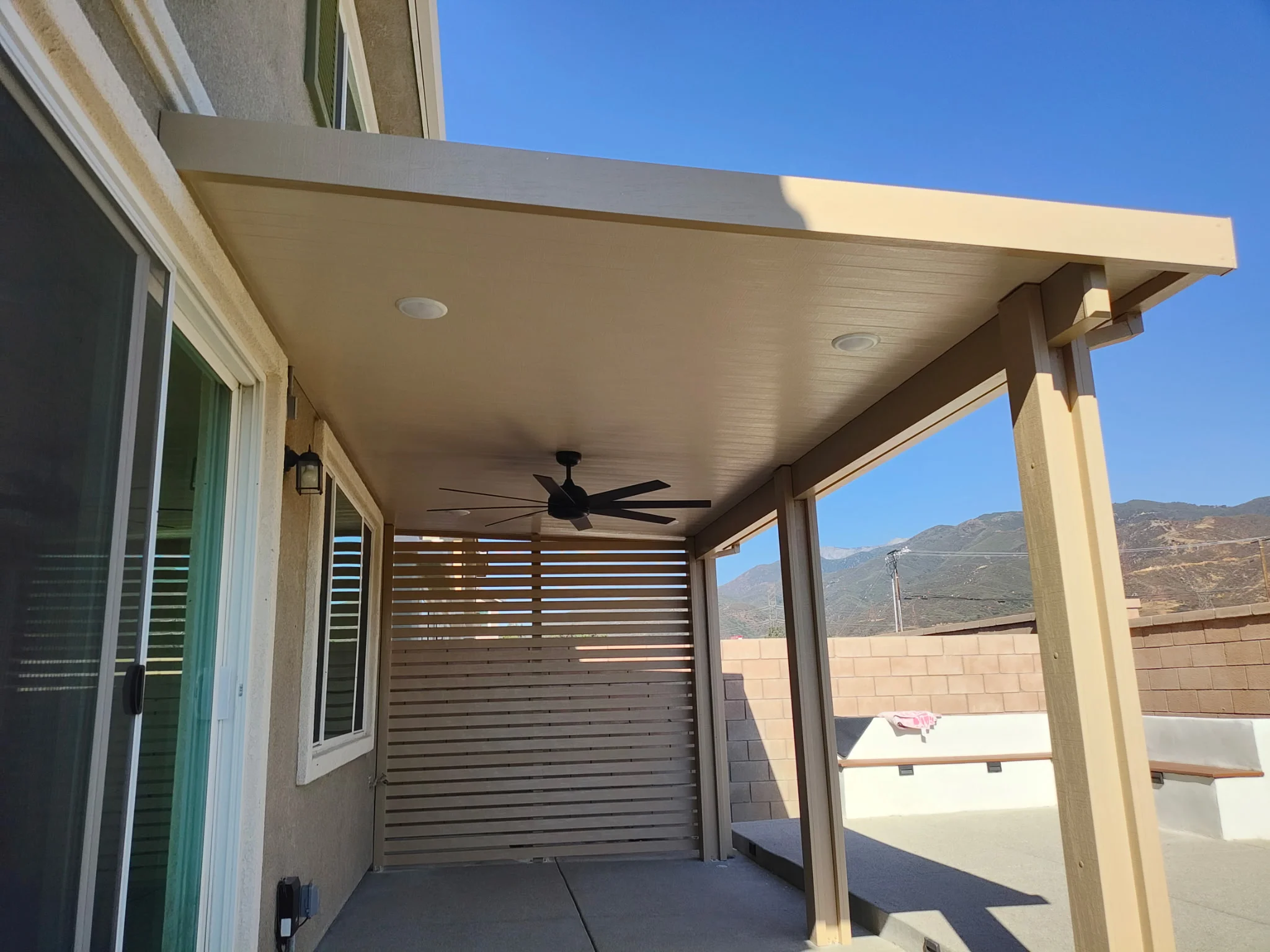 Covered patio with composite ceiling, ceiling fan, and horizontal wood slat privacy screen
