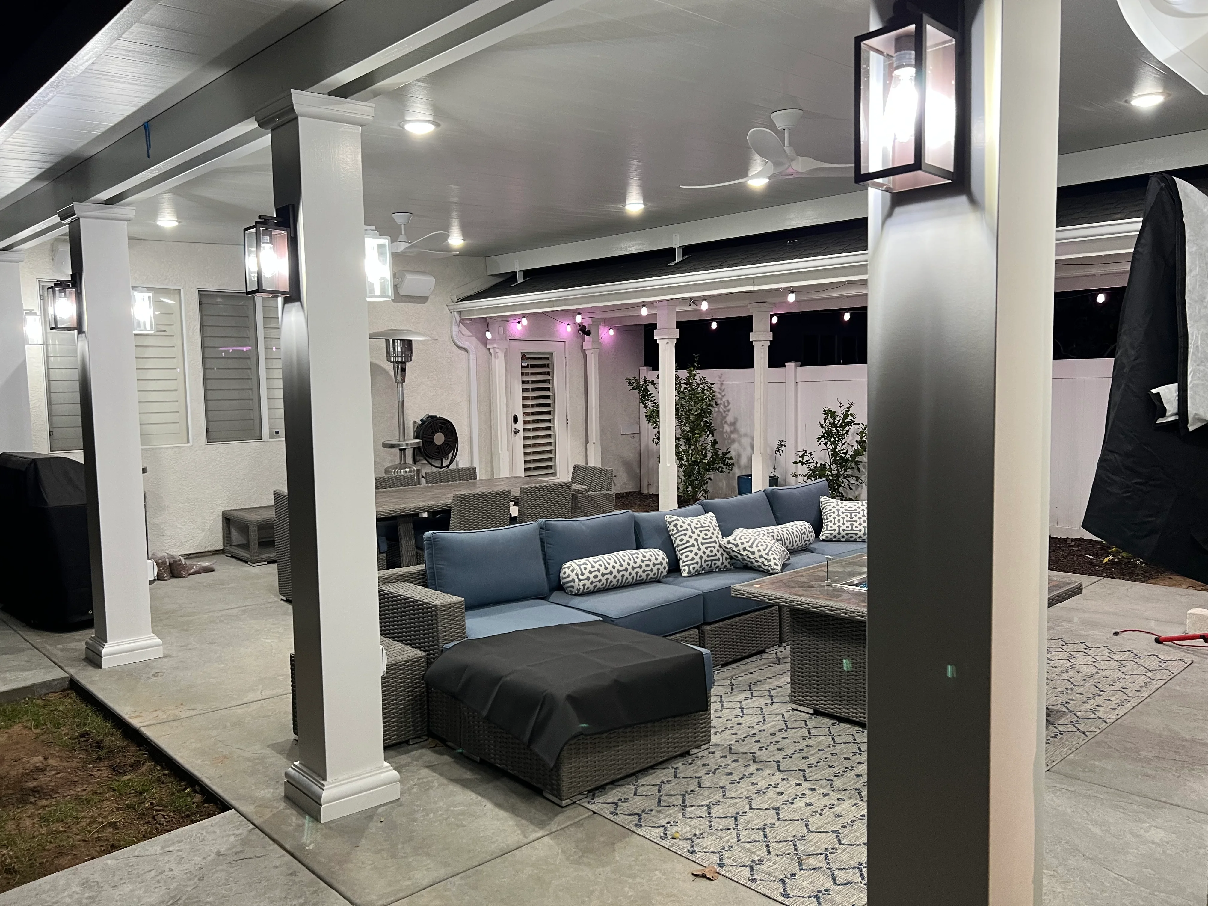 Nighttime view of illuminated patio cover with white columns, seating area, and ambient lighting