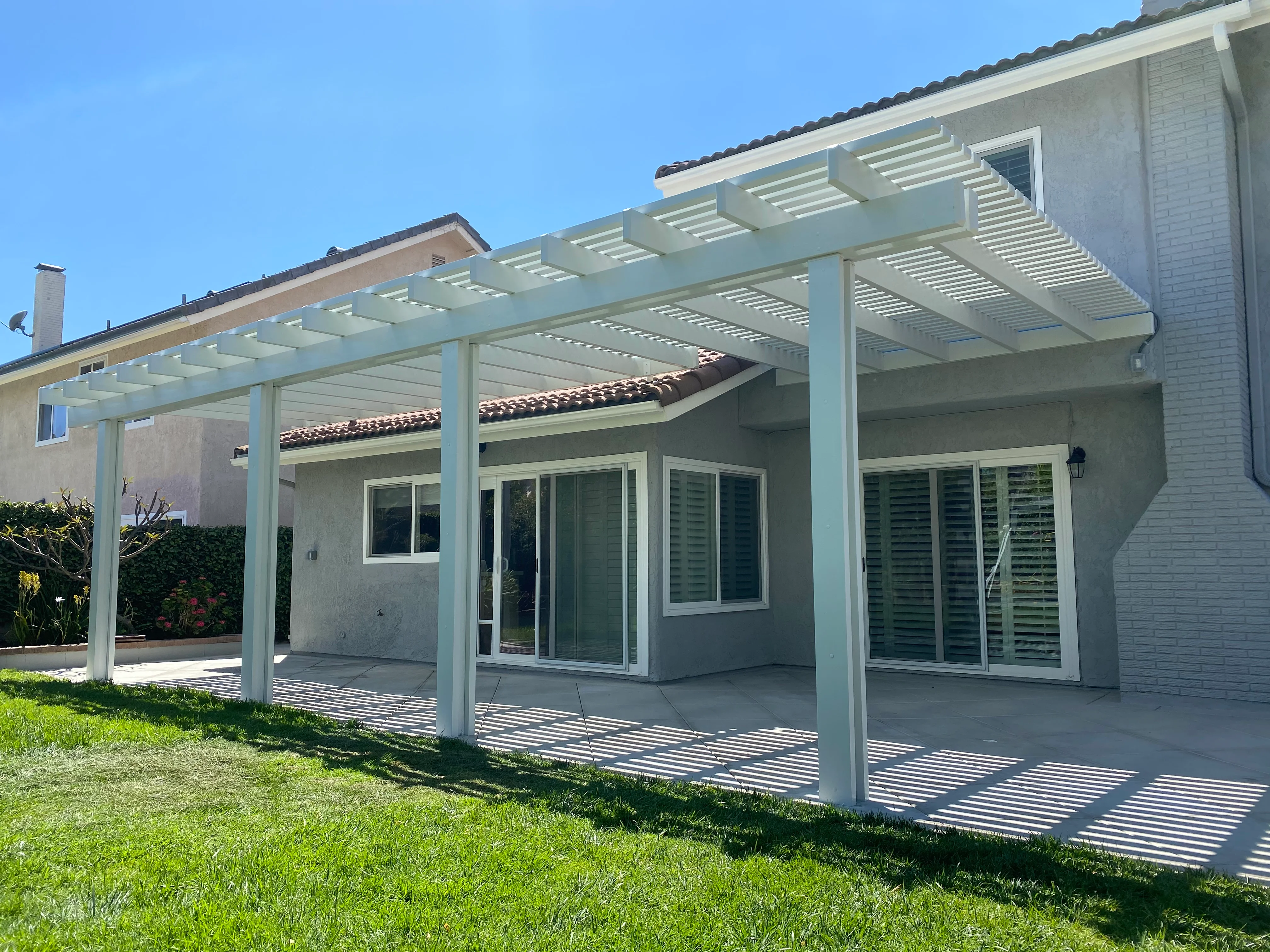 White aluminum pergola with louver slats over concrete patio attached to home