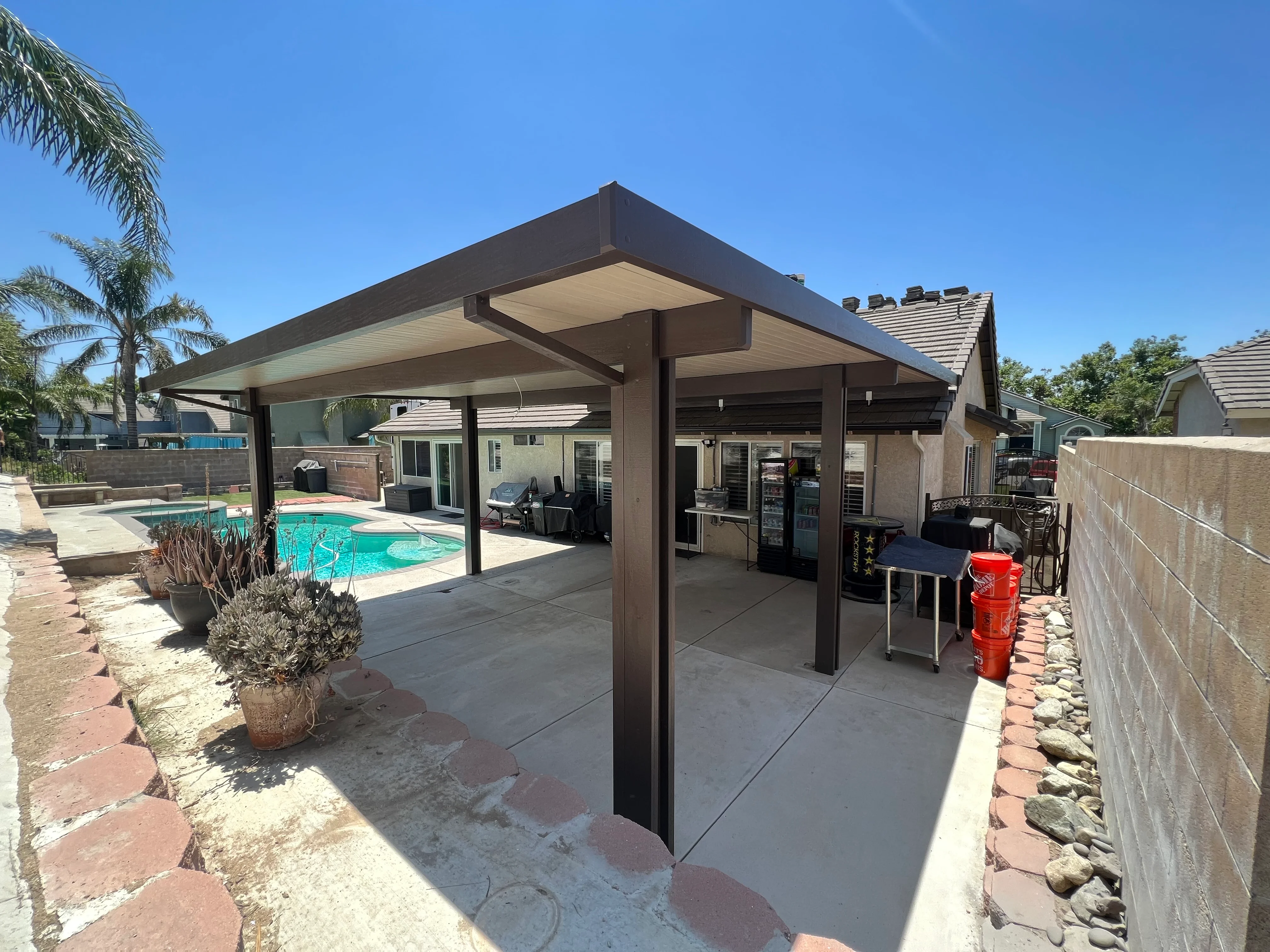 Brown aluminum patio cover with peaked roof over concrete pad and pool area