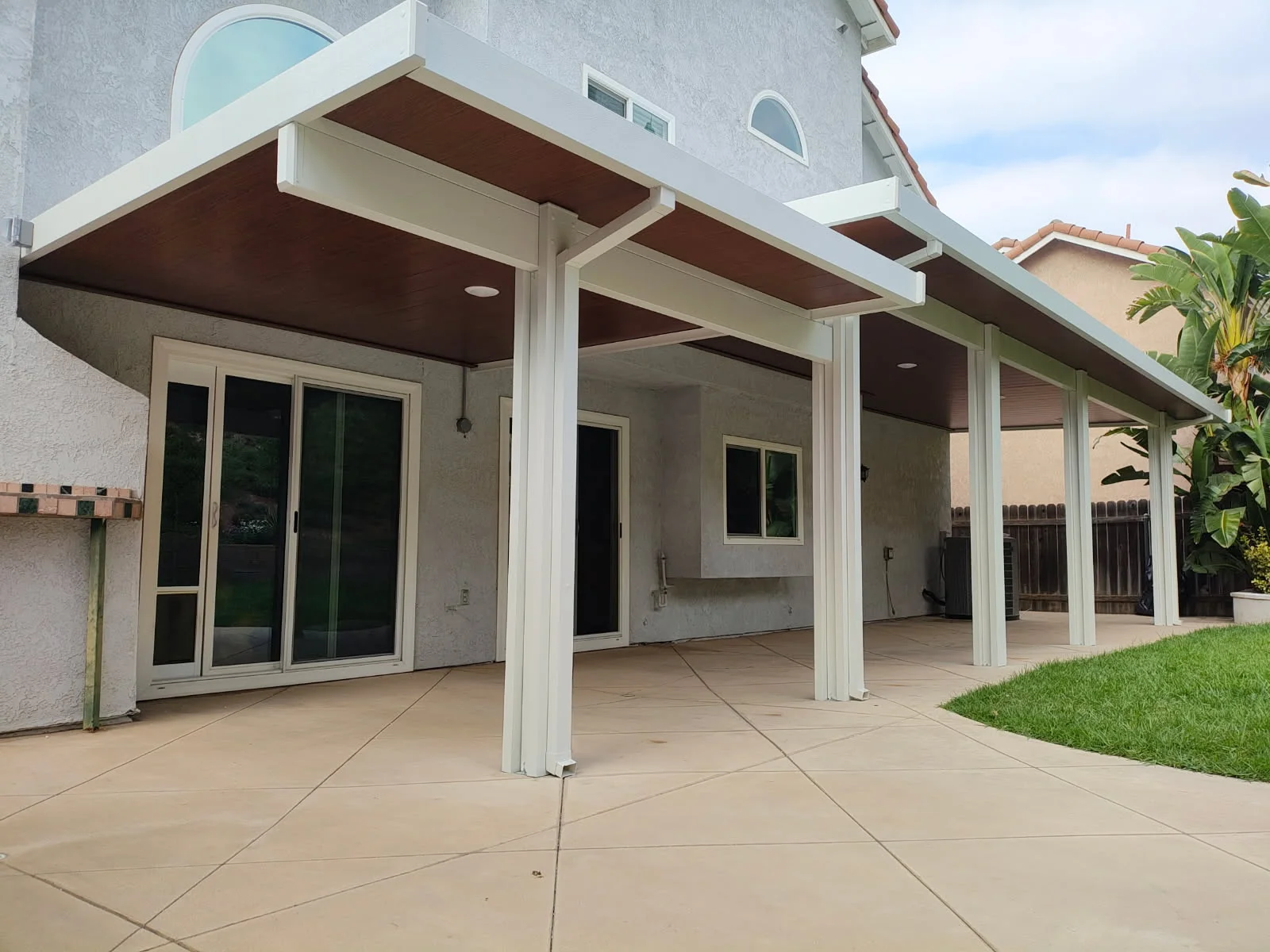 White aluminum patio cover with brown soffit over concrete patio and glass doors