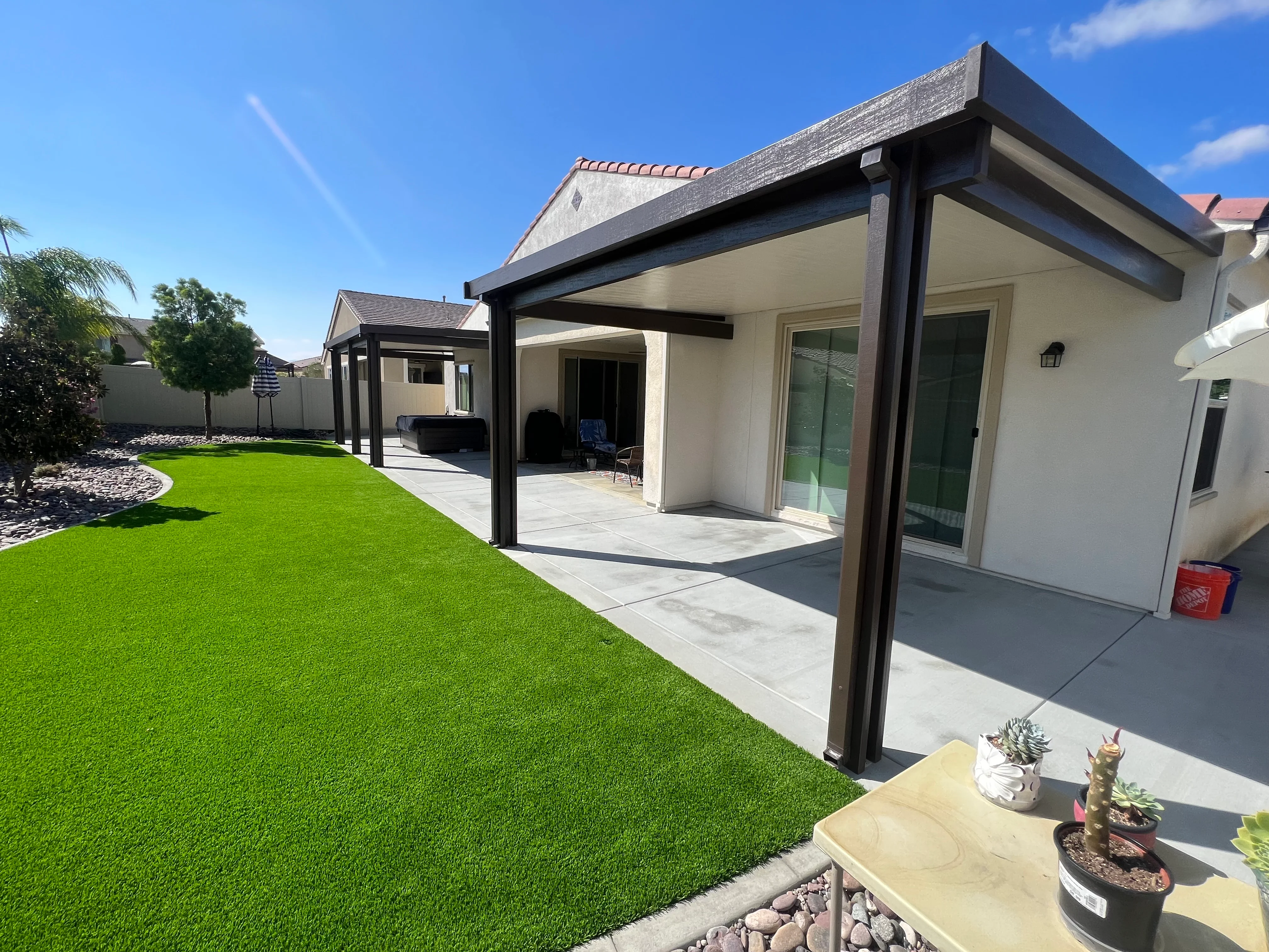 Black aluminum patio cover with white ceiling over concrete patio and green artificial turf lawn