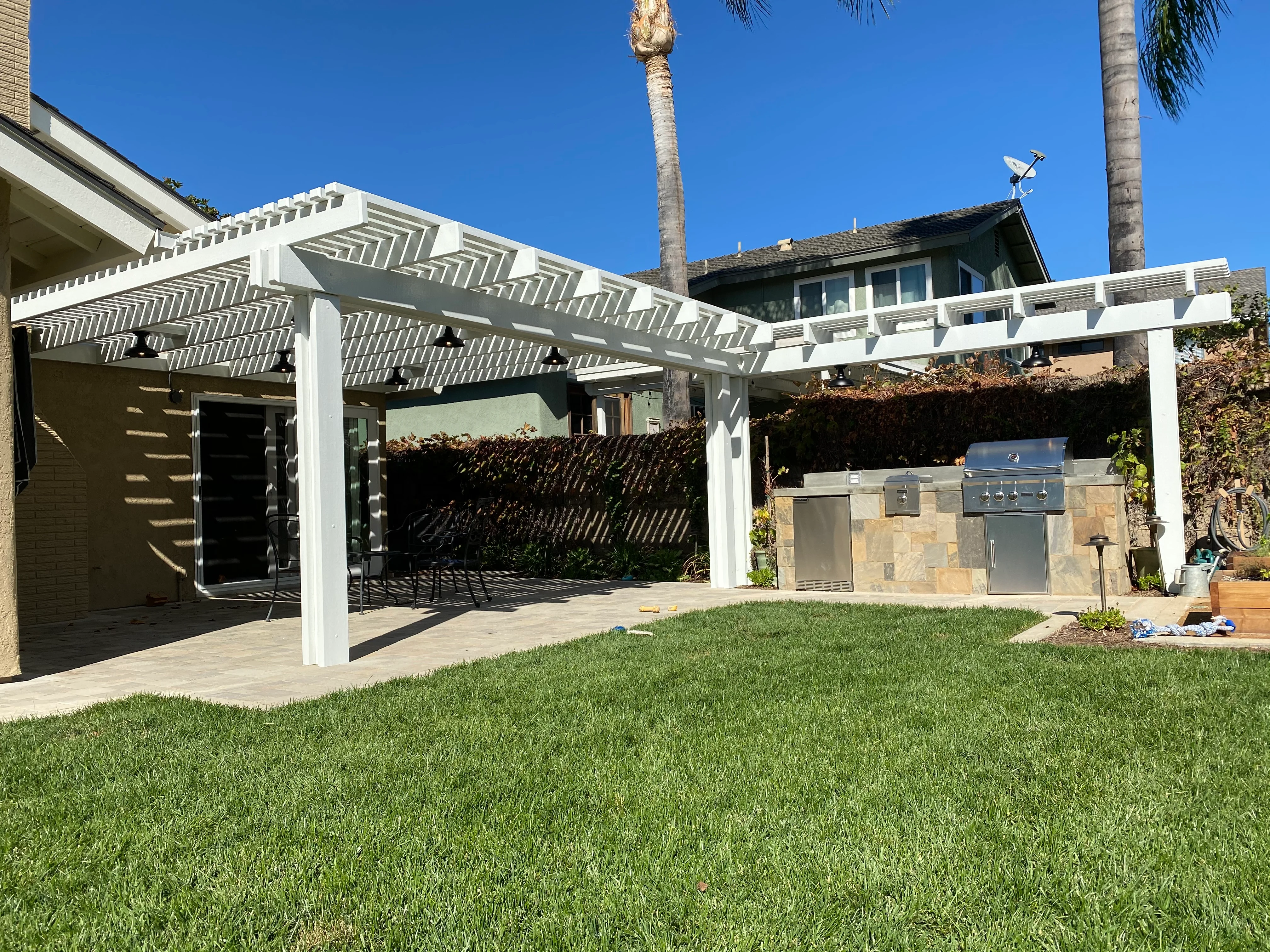 White pergola with geometric lattice roof over patio with outdoor kitchen and grill