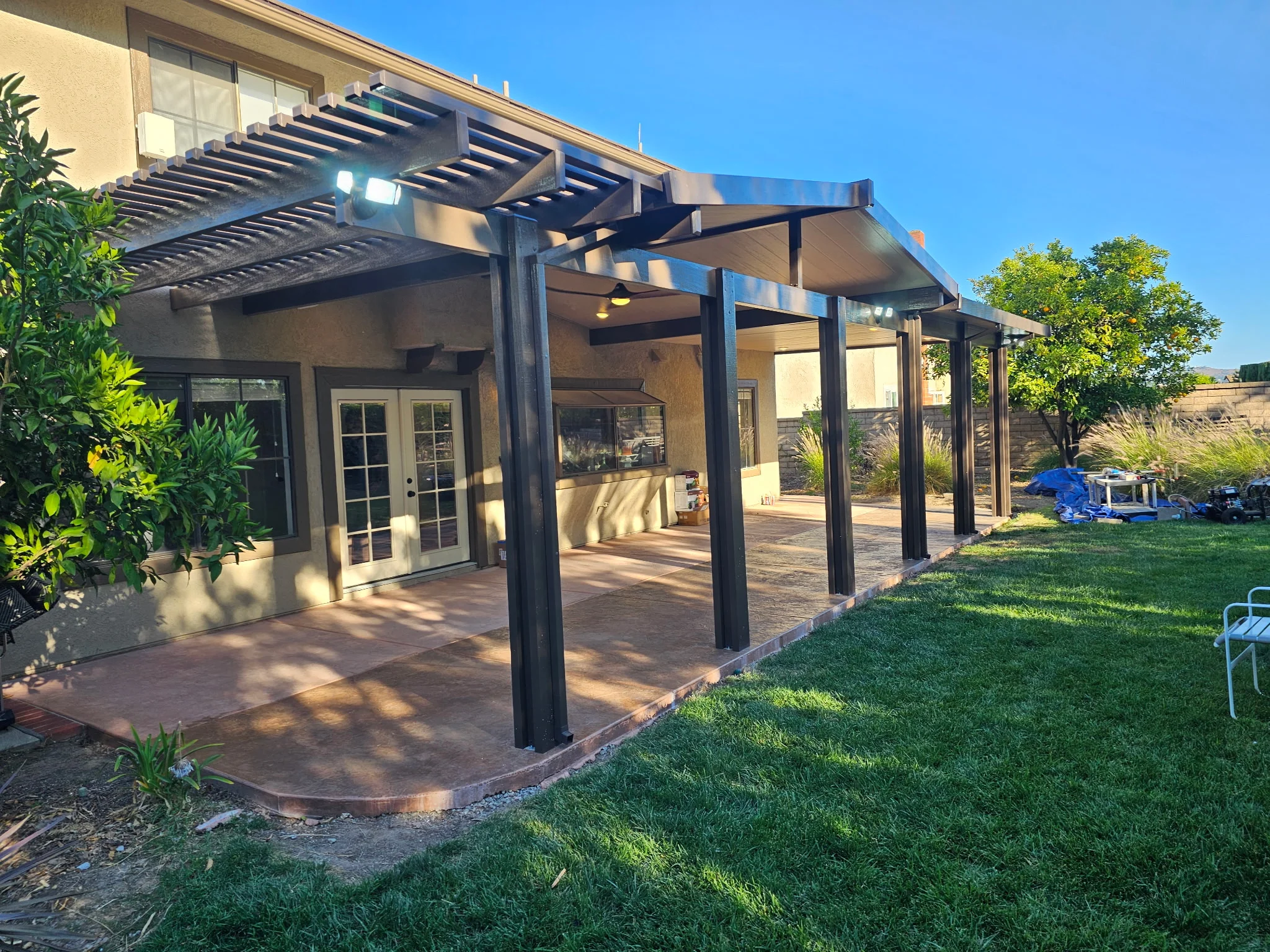 Modern black pergola patio with louvered roof attached to home with French doors