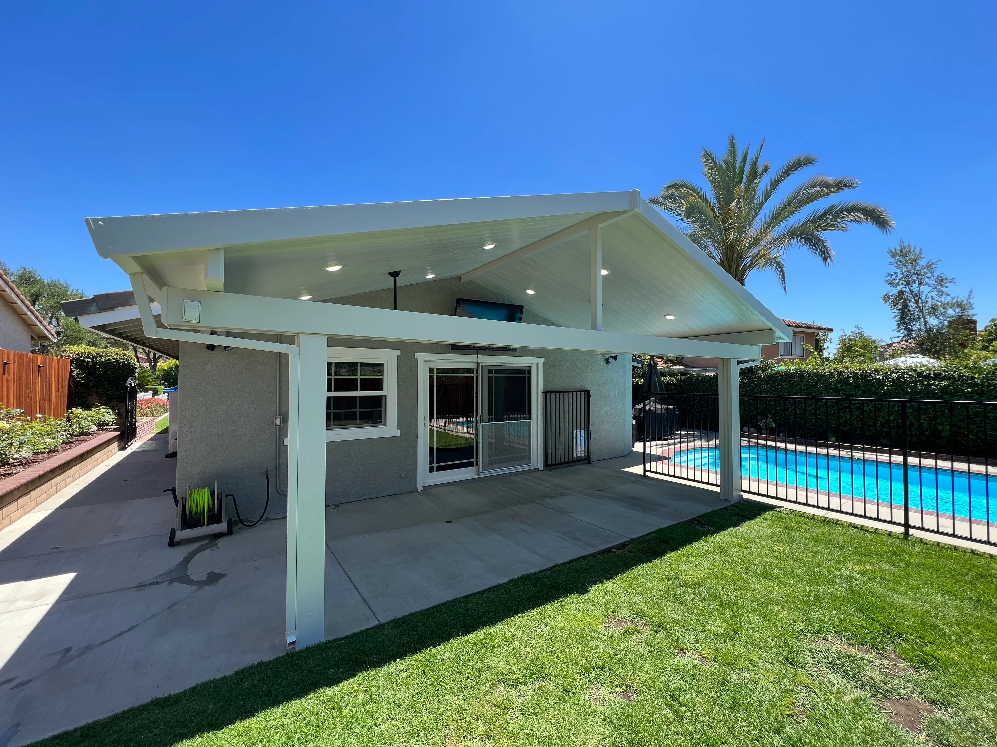 Modern white patio cover with angled roof over concrete pad near swimming pool